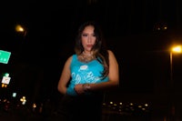 a woman in a blue tank top standing on a street at night