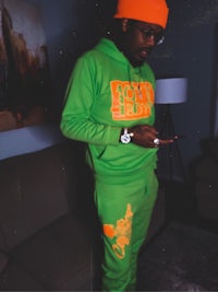 a man in a green and orange tracksuit standing in a living room