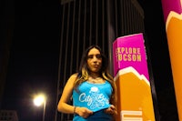 a woman in a blue tank top standing in front of a pole